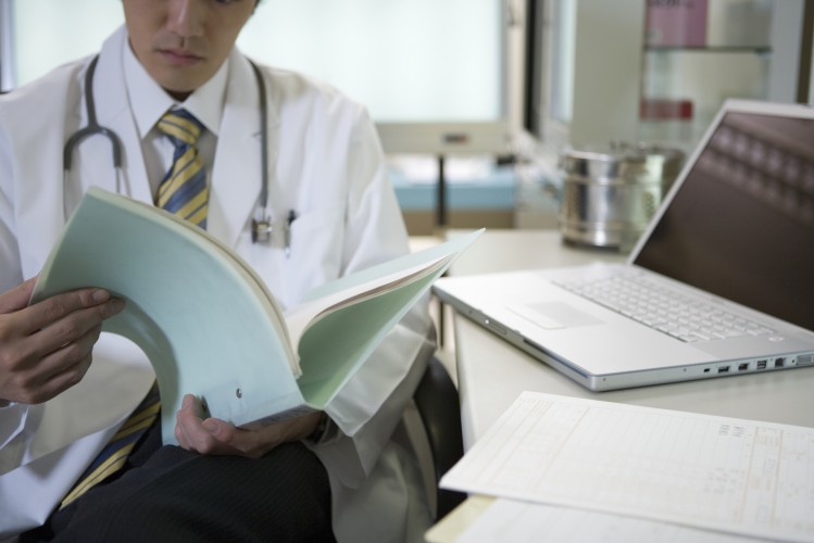 doctor-reading-medical-records-beside-laptop
